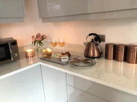 A modern kitchen with high-gloss grey cabinets, a dark tiled floor, and copper-coloured accessories.