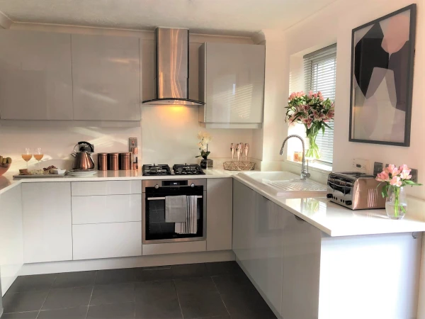 A modern kitchen with high-gloss grey cabinets, a dark tiled floor, and copper-coloured accessories.