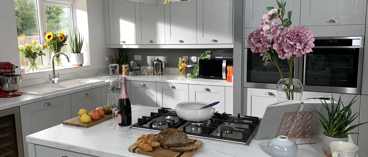 A bright, modern shaker-style kitchen with light grey cabinets, a large central island, and marble-effect countertops.