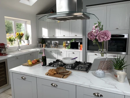 A bright, modern shaker-style kitchen with light grey cabinets, a large central island, and marble-effect countertops.