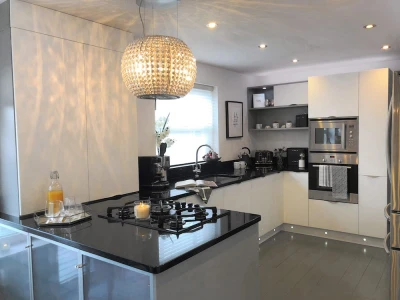 A modern kitchen with glossy white cabinets, black countertops, and a large, spherical crystal chandelier.