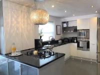 A modern kitchen with glossy white cabinets, black countertops, and a large, spherical crystal chandelier.