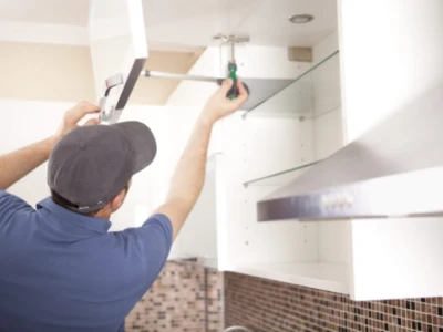 A worker uses a screwdriver to install a white kitchen cabinet door.
