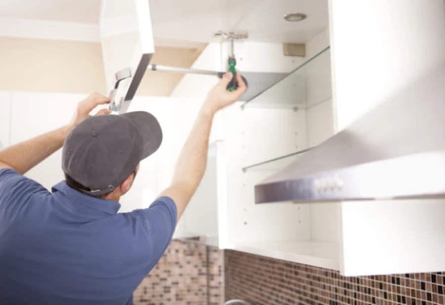 A worker uses a screwdriver to install a white kitchen cabinet door.