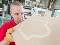 Warehouse worker checking unfinished kitchen door panel in production workshop during cabinet manufacturing process.