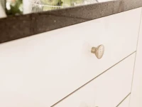 Gold finish doorknob on white kitchen drawers, decorative handle accent and modern hardware detail.